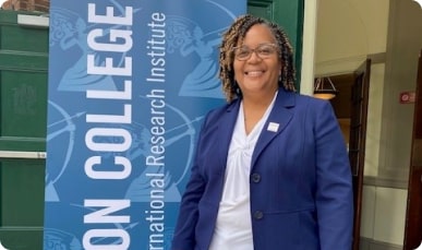 A woman in a blue suit and glasses stands in front of a poster.